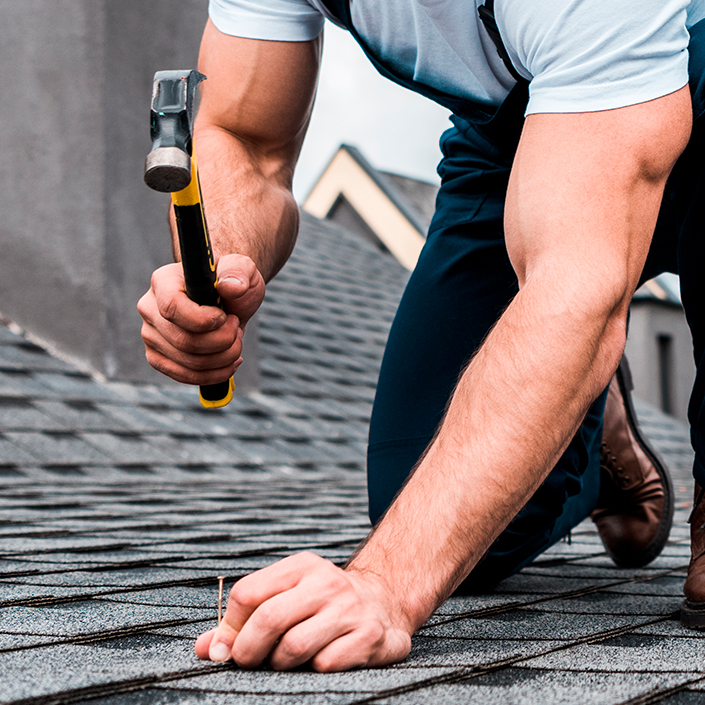 Man Hammering a nail into a roof to hold shingles