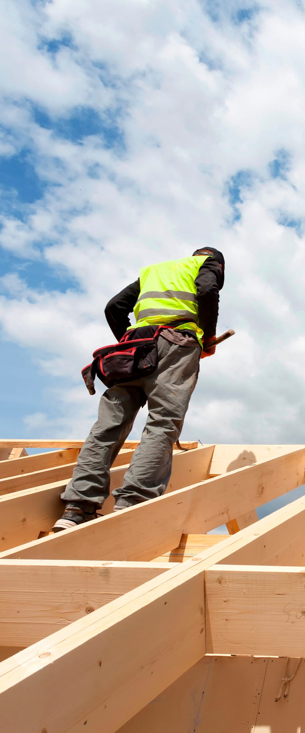 roofer wearing a security vest on the top of a wooden roof structure