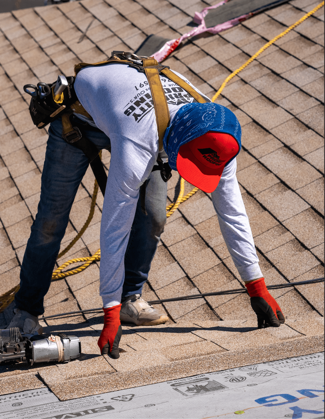 Roofer on top of a red shingle roof placing shingles.